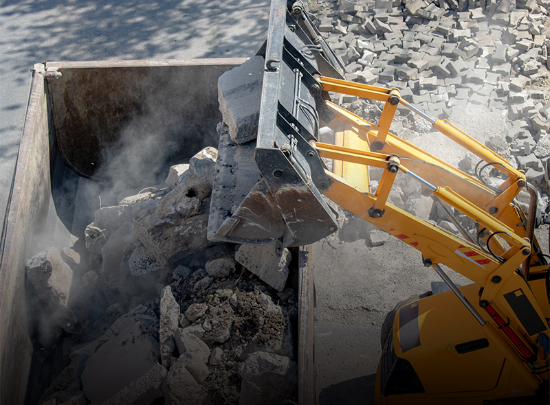 Gravel and rocks being dumped into a dumpster.